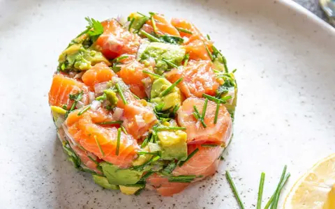 Un délicieux tartare saumon avocat, frais et coloré, garni de ciboulette et servi avec un quartier de citron.