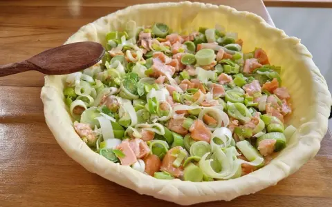 Préparation d'un plat végétarien : une tarte garnie de saumon et de poireaux coupés, prête à être cuite.