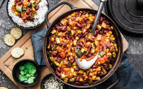 Un plat de chili végétarien copieux avec des haricots rouges, du maïs et des courgettes, servi avec du riz blanc.