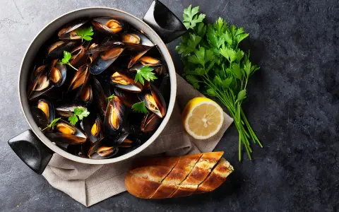 Un plat de moules au rosé, garni de persil frais, avec un quartier de citron et une baguette à l'ail.