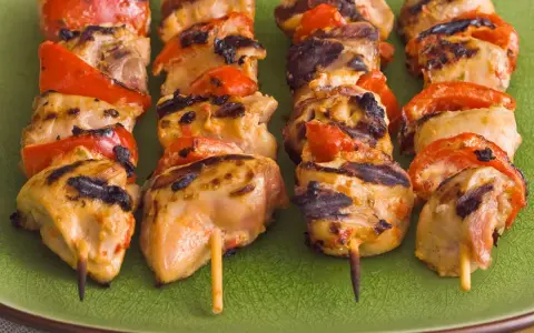 Brochettes de poulet grillé avec poivrons rouges sur une assiette verte. Parfait pour savoir quoi servir avec des brochettes de poulet.