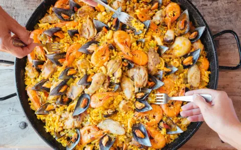 Un plat généreux de poulet paella, garni de crevettes et de moules, prêt à être dégusté par plusieurs mains.