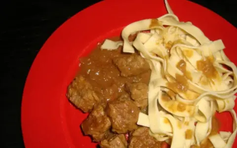 Un plat de pâtes fraîches avec un riche boeuf vindaloo, servi sur une assiette rouge vif.