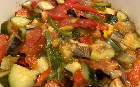 Un plat coloré de ratatouille niçoise, avec des morceaux de courgettes, aubergines, tomates et poivrons mijotés.