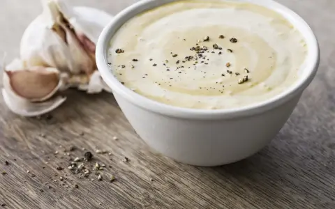 Sauce césar sans oeuf crémeuse, parsemée de poivre noir, avec une tête d'ail en arrière-plan sur fond de bois.