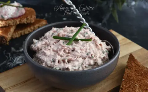 Un bol de rillettes de thon crémeuses, garni de ciboule, prêt à être tartiné sur des toasts grillés.