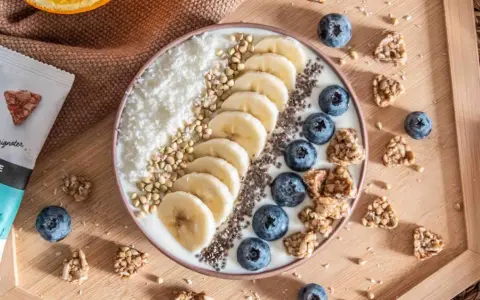 Un bol de smoothie aux fruits, bananes, myrtilles, noix de coco râpée et graines. Idéal pour manger sain le midi, avec des encas du supermarché.