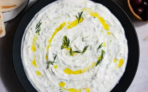 Un plat de tzatziki crémeux, garni d'aneth frais et d'huile d'olive. Parfait pour accompagner votre recette de tzatziki maison.
