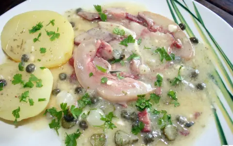 Tête de veau en sauce avec des pommes de terre et des câpres, garnie de persil frais.