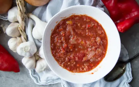 Un bol de salsa facile, avec des tomates, des oignons et des poivrons rouges. Des gousses d'ail et un oignon sont disposés autour.