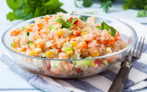 Salade quinoa colorée avec des dés de tomates, carottes, concombre et maïs, garnie de feuilles de menthe fraîche.