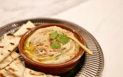 Un bol de baba ganoush crémeux, garni de persil frais et d'un filet d'huile d'olive, servi avec des pains pita grillés.