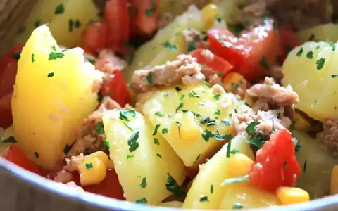 Salade de pommes de terre, thon, tomates et maïs, garnie de persil frais. Un plat simple et savoureux.