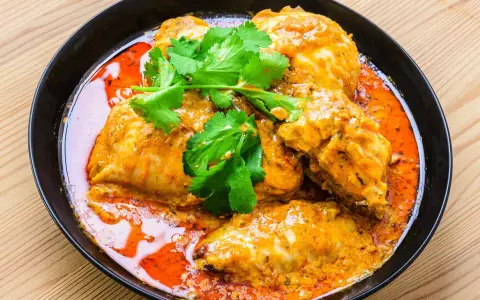 Un plat de poulet vindaloo, un curry indien épicé, servi dans un bol noir avec de la coriandre fraîche.