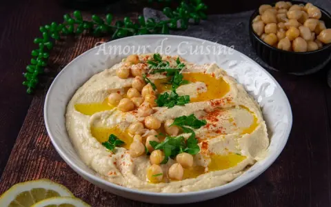 Un plat de houmous crémeux, garni de pois chiches, persil et paprika. Parfait pour découvrir 7 recettes de houmous maison.