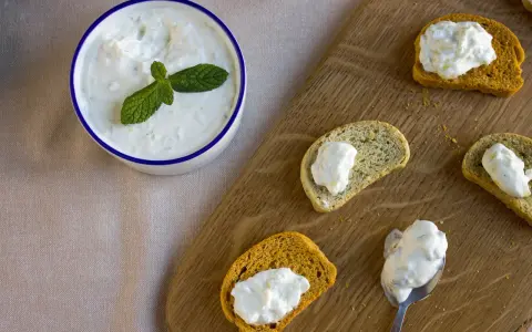 Un bol de crème tzatziki frais, garni de menthe, est servi avec des toasts.