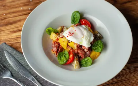 Salade colorée avec œuf poché, tomates cerises, lardons et quelques feuilles de salade légumes verts.