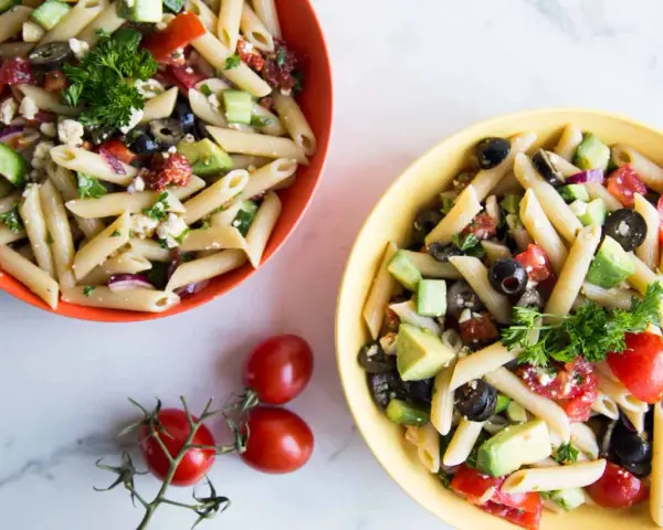 Deux bols de salade de pâtes méditerranéenne colorée, garnie de feta, olives, tomates et avocat.