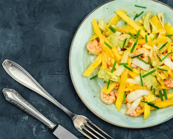 Salade colorée avec des crevettes, de l'avocat et des bâtonnets de mangue, garnie de ciboule. Un délice frais et fruité.