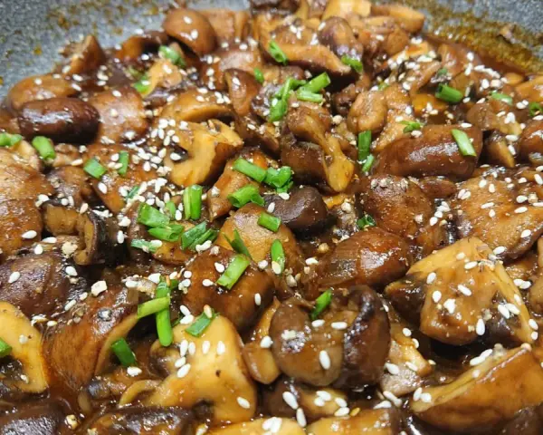 Champignons caramélisés chinois, brillants et appétissants, saupoudrés de graines de sésame et de ciboule fraîche.