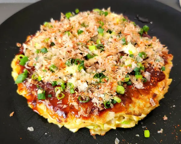 Un délicieux okonomiyaki, un plat emblématique du repas japonais maison, garni d'oignons verts et de flocons de bonite.