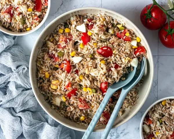 Un grand bol de salade de riz thon, garnie de tomates, maïs et œufs durs. Parfait pour un repas frais et léger.