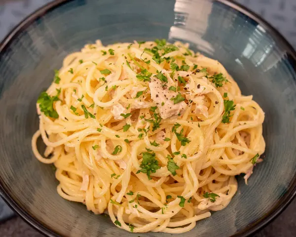 Un plat de pâtes au thon, garni de persil frais et de poivre noir, servi dans un bol bleu.