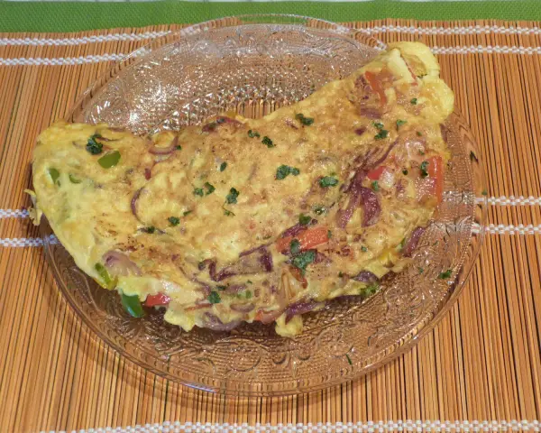 Une savoureuse omelette mexicaine garnie d'oignons rouges, de poivrons et d'herbes fraîches, servie sur une assiette en verre.