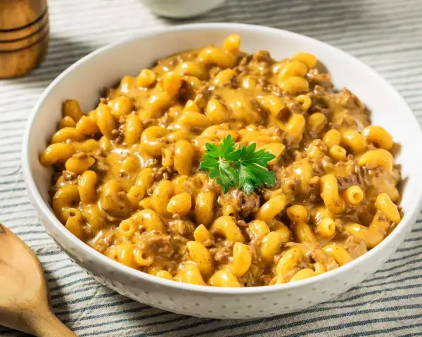 Un bol de macaroni au fromage crémeux avec du bœuf haché, garni de persil. Un plat parfait pour un dîner rapide et facile.