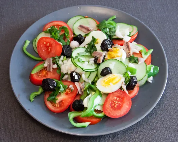 Salade niçoise colorée avec tomates, concombres, œufs, olives noires et anchois.