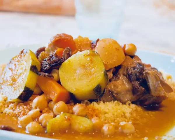 Un plat généreux de couscous algérien avec légumes, pois chiches, raisins secs et viande mijotée dans une sauce savoureuse.