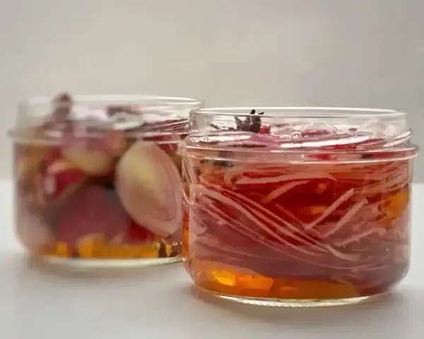 Deux bocaux de pickles d'oignon rouge, l'un avec des oignons entiers, l'autre avec des lamelles fines, baignant dans une marinade ambrée.