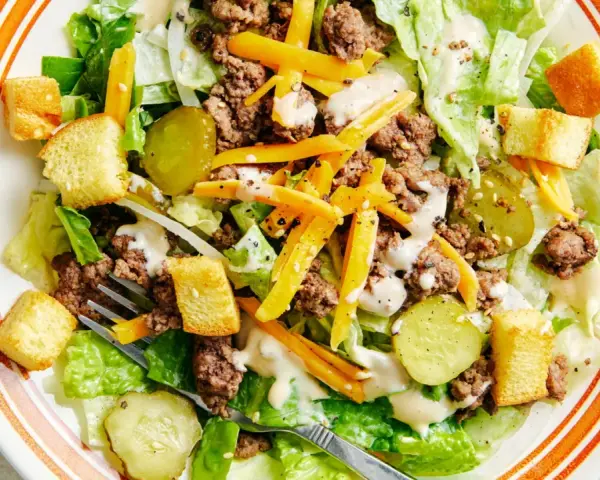 Salade Big Mac avec laitue, bœuf haché, fromage râpé, croûtons et cornichons, arrosée d'une sauce crémeuse.