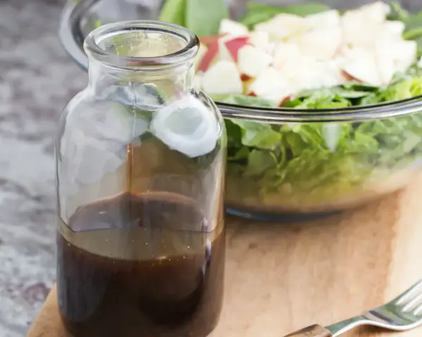 Bouteille de sauce salade facile, prête à être versée sur une salade fraîche et croquante dans un bol en verre.