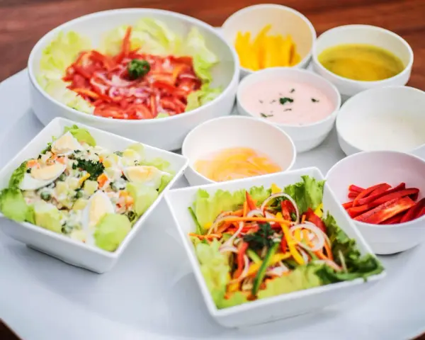 Assortiment de salades colorées avec plusieurs options de sauce pour salade, dont une rose et une verte.