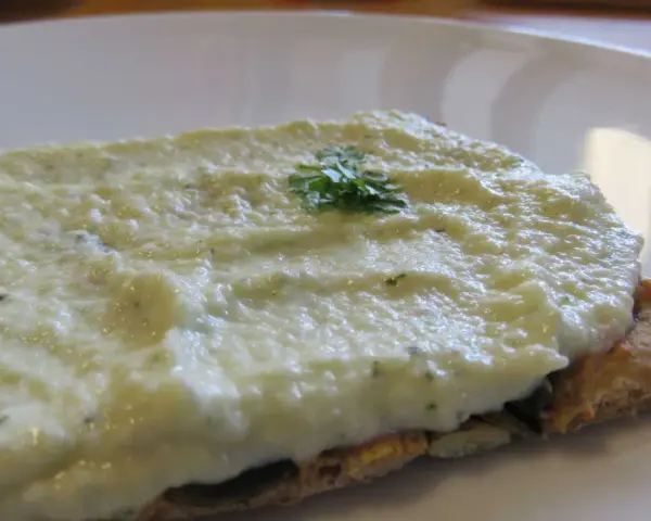 Houmous de courgette crémeux sur une tranche de pain complet, garni d'une touche de persil frais.