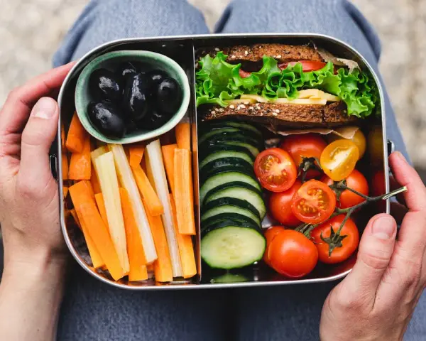Un bento sain avec sandwich, bâtonnets de carottes et céleri, tomates cerises, concombres et olives noires.