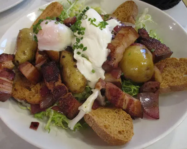 Une généreuse salade vosgienne avec des pommes de terre, lardons, œuf poché et croûtons sur un lit de verdure.