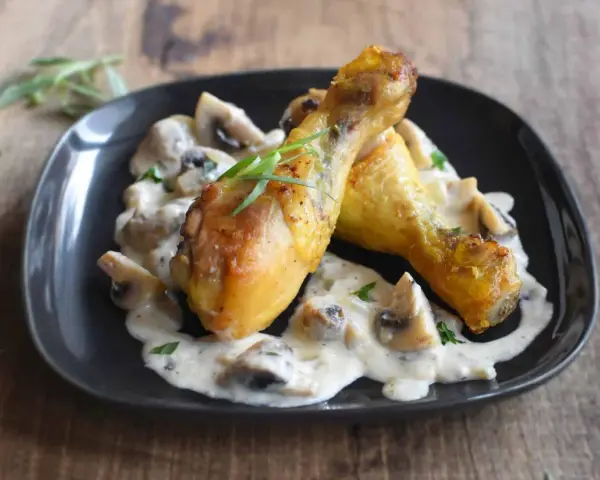 Deux pilons de poulet dorés baignent dans une sauce crémeuse aux champignons, garnie d'herbes fraîches. Un délice de poulet à la crème.