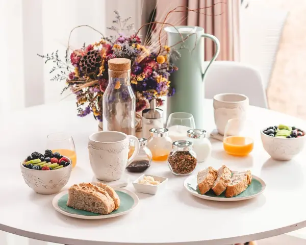 Un délicieux déjeuner vegan avec fruits frais, pain artisanal, granola et jus d'orange, présenté sur une table blanche.