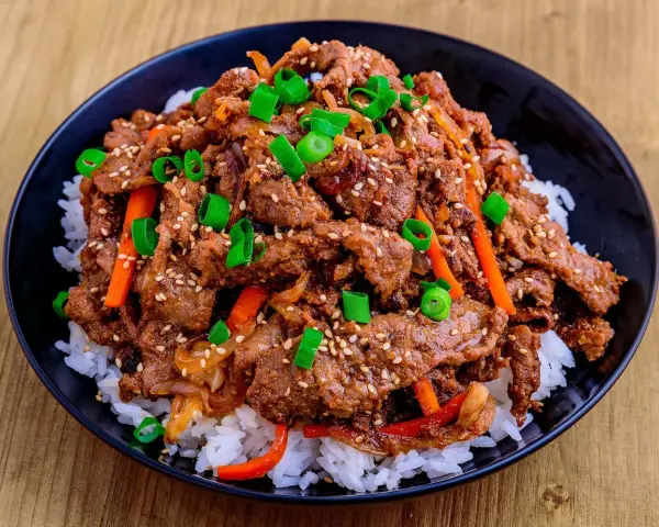 Un bol de riz blanc garni de boeuf bulgogi mariné, de julienne de carottes et d'oignons verts ciselés, parsemé de graines de sésame.