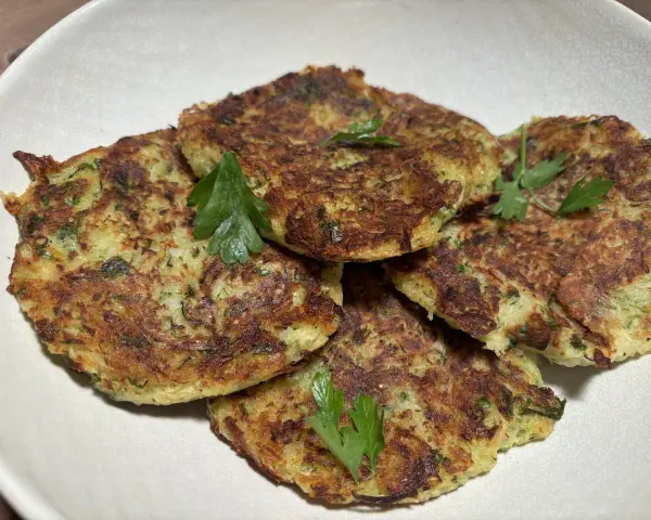 Galettes dorées de courgette et pomme de terre, garnies de persil frais, prêtes à être dégustées.