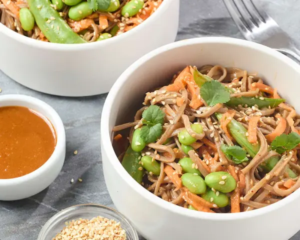 Pâtes soba aux edamames, carottes râpées et coriandre, servies avec une sauce crémeuse. Un délice sain et coloré.