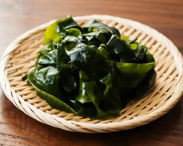 Un tas d'algue japonaise verte et brillante repose dans un panier en osier sur une table en bois.