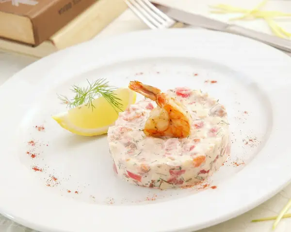 Délicieux tartare de crevette thaï, garni d'une crevette grillée et d'une tranche de citron, sur une assiette blanche.