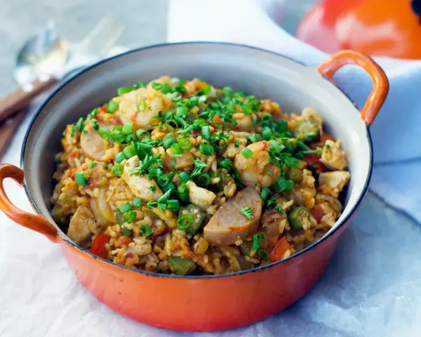 Un plat de jambalaya coloré, garni de crevettes, poulet, saucisse et oignons verts. Une recette savoureuse à découvrir.