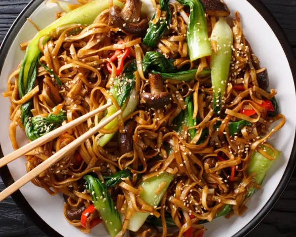 Un plat de chow mein appétissant avec des nouilles, des légumes verts croquants, des champignons et des poivrons rouges, saupoudré de graines de sésame.