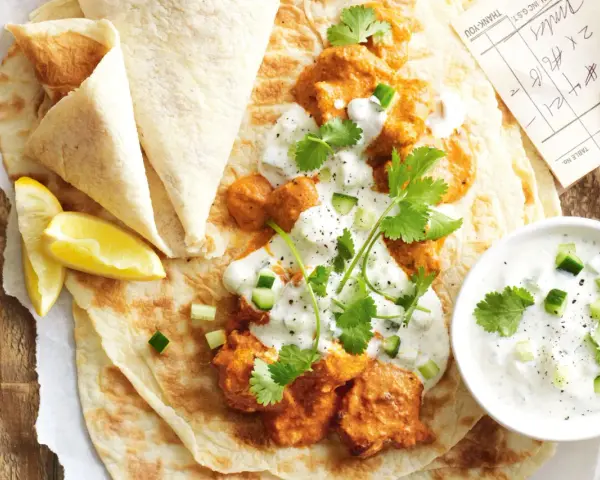 Un plat de butter chicken crémeux servi sur du pain naan avec du raïta et des quartiers de citron.