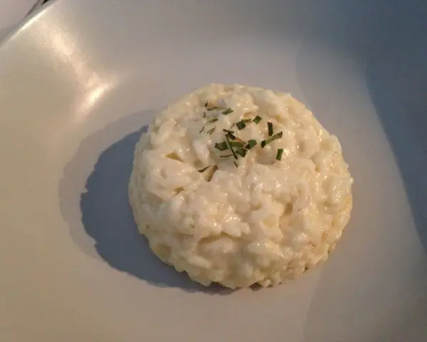 Un crémeux risotto coco, parsemé de ciboulette fraîche, repose sur une assiette claire.