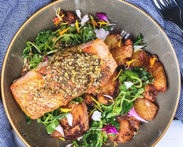 Un filet de saumon croustillant, garni de graines, servi avec des pommes de terre rôties et une salade verte. Un accompagnement poisson savoureux et coloré.